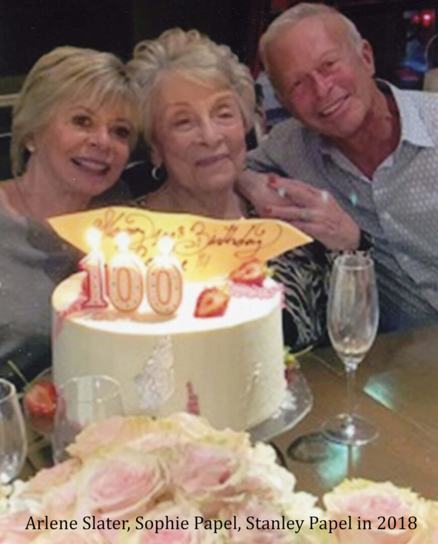 Three people sitting at a table with a cake.