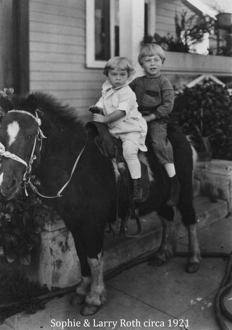 Two young boys riding on a horse in front of a house.